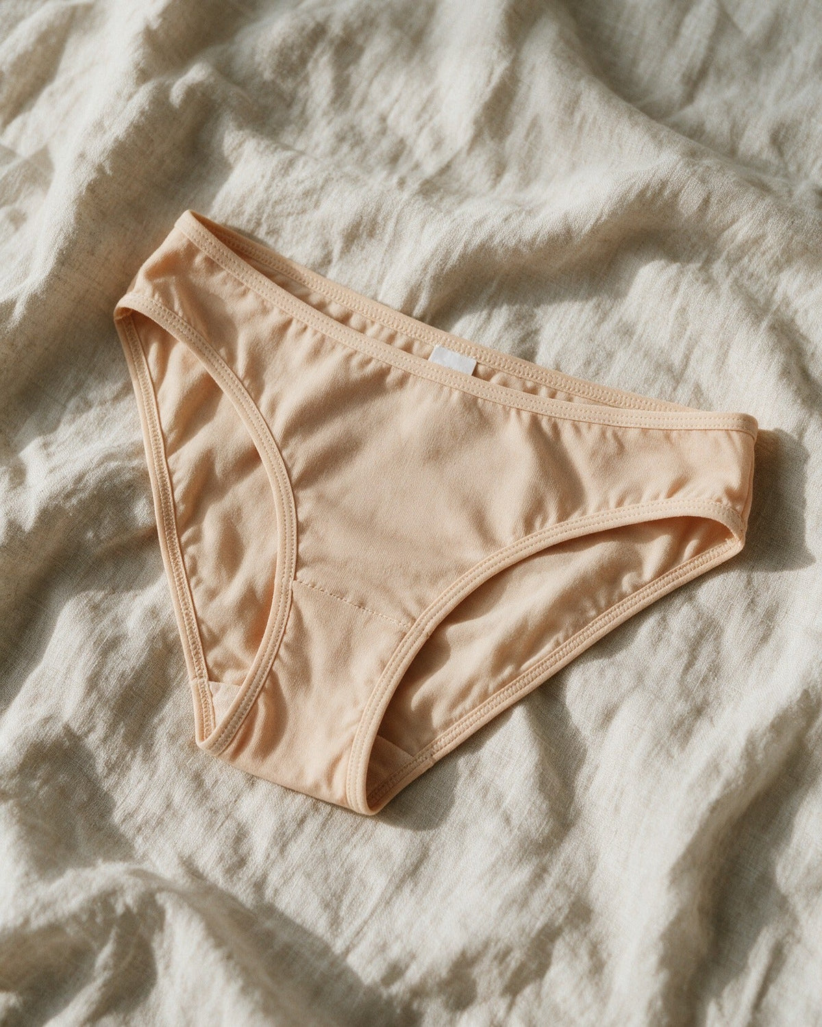 Elodie women's bamboo bikini brief in Beige, laid flat on linen