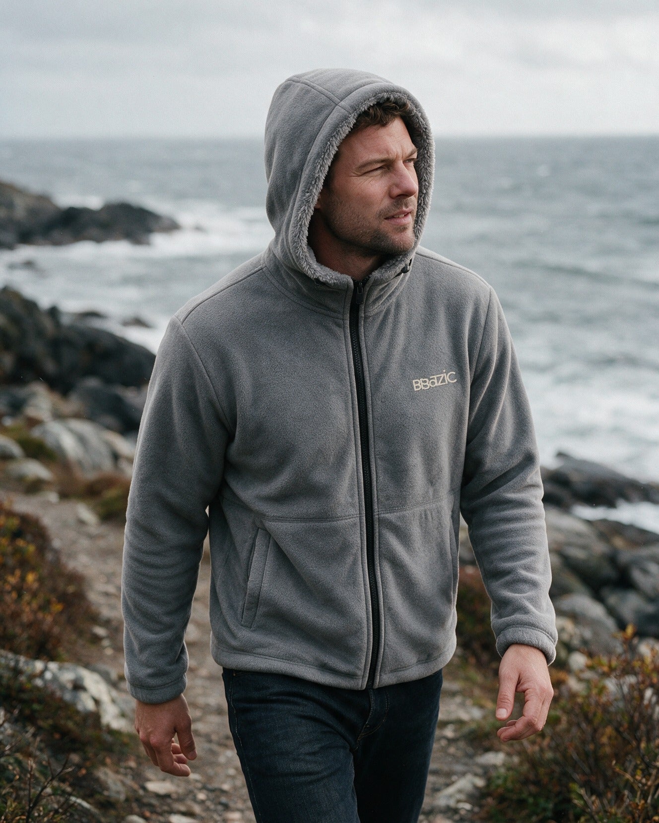 Man on a coastal trail wearing the grey Norway fleece hoodie with the hood up
